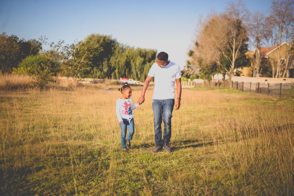 A father walking hand in hand with his young daughter across a grassy field in Pretoria