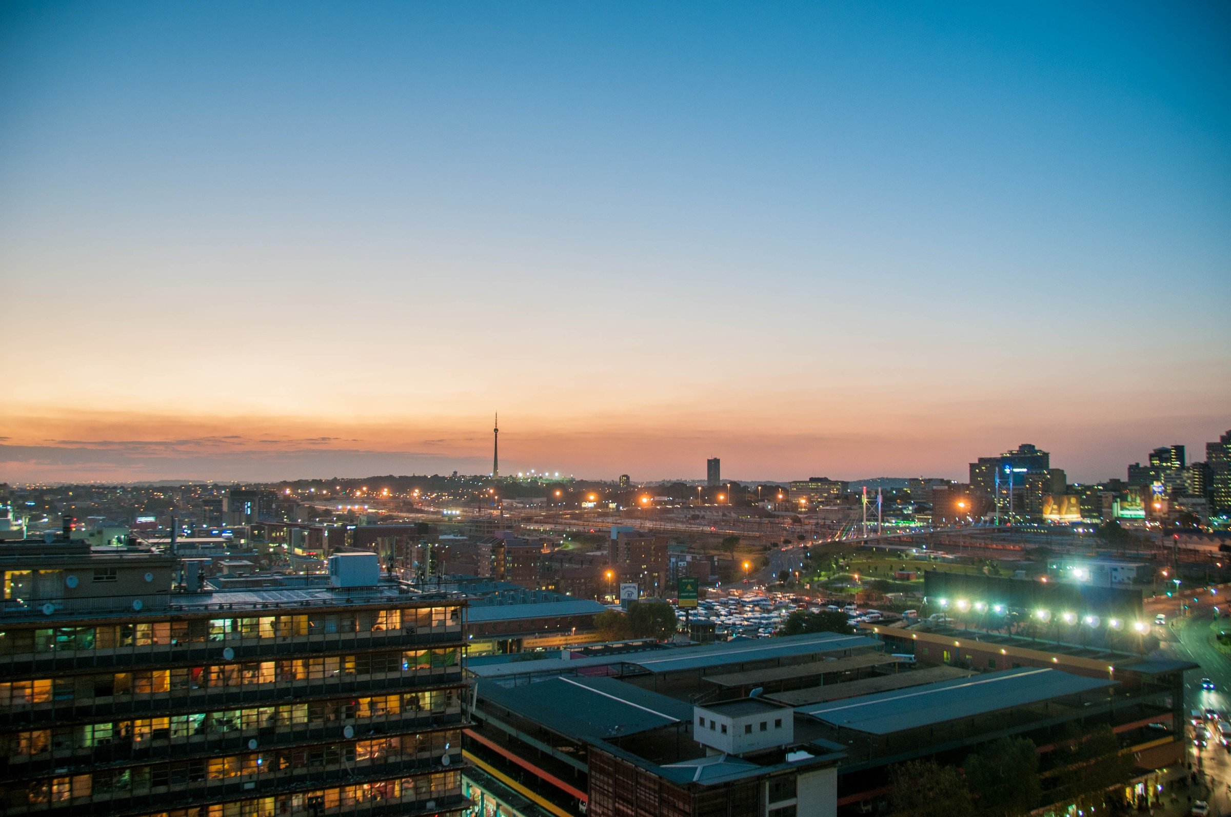 Johannesburg city centre at twilight, with street lights glowing beneath an orange and blue sky
