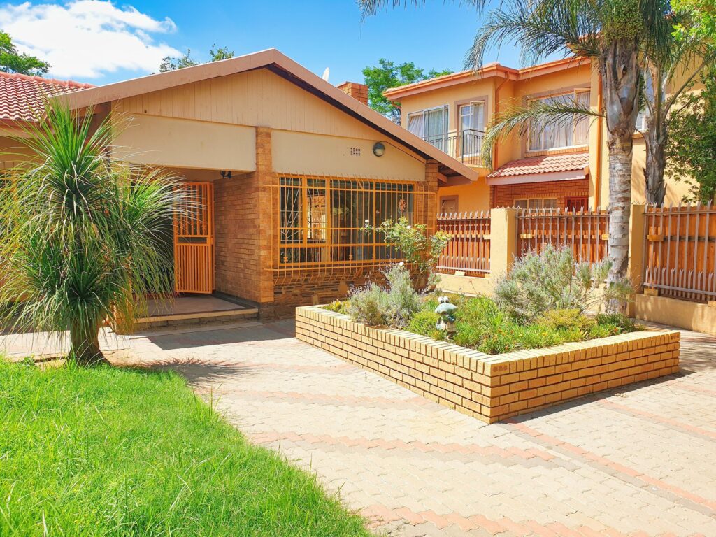 A face-brick suburban house with burglar bars, palm trees and a paved garden in Pretoria